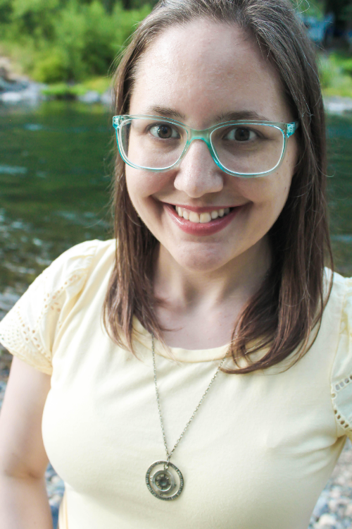 Headshot of Cindy Baldwin, brunette hair, green glasses, and a yellow shirt in front of a river.